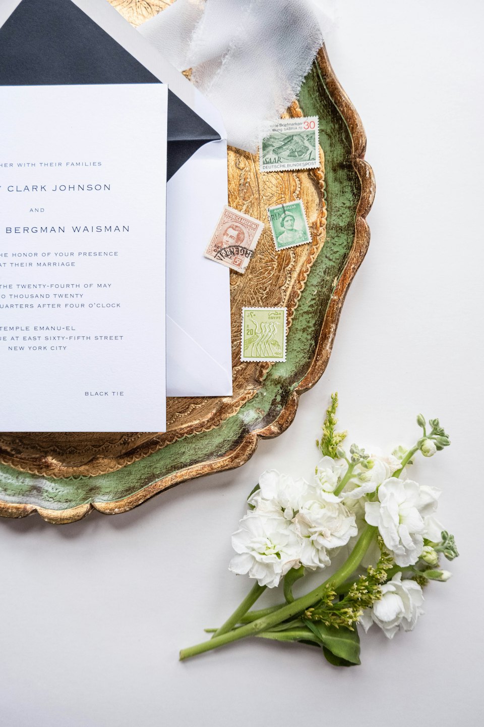 Conjunto de invitaciones de boda dispuestas en una ornamentada bandeja dorada y verde.
